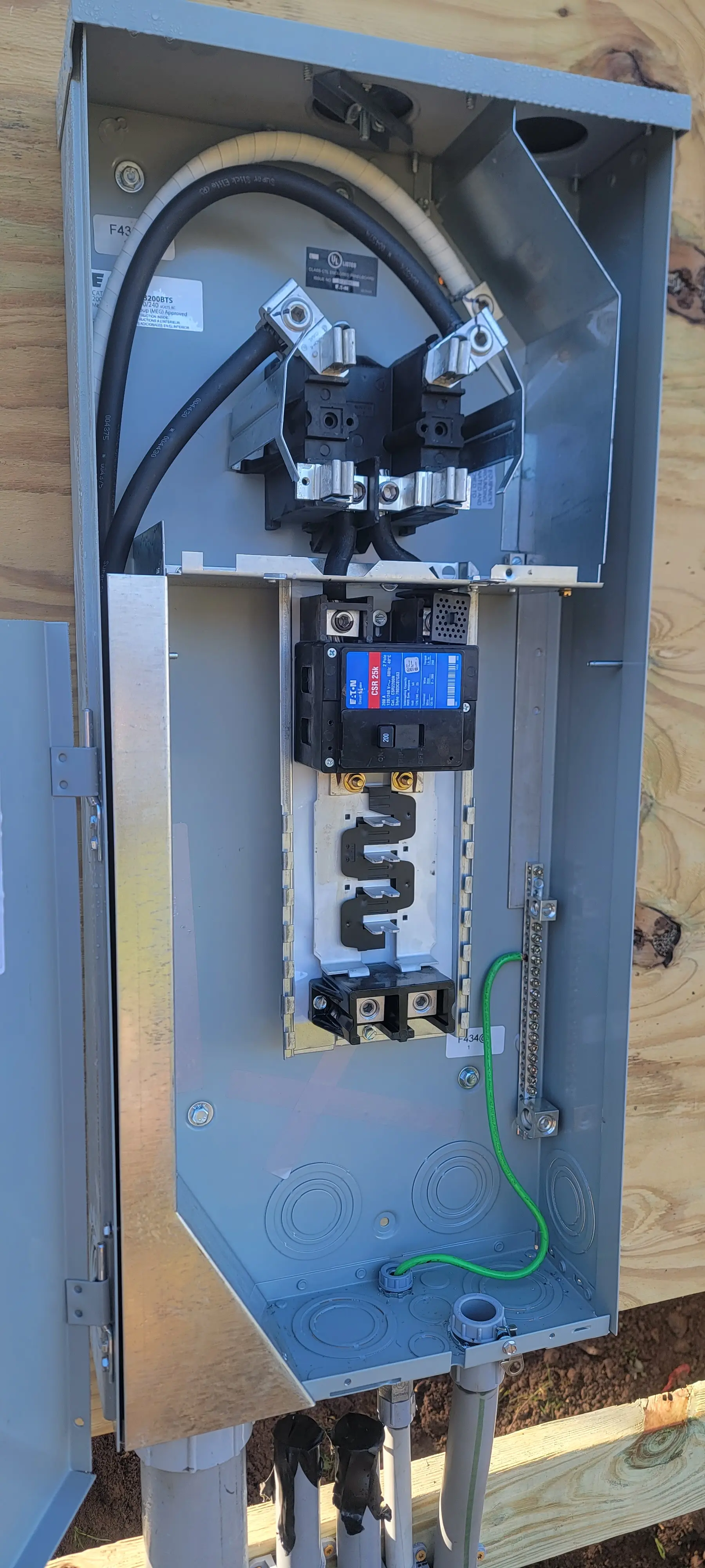 Outdoor residential electrical panel installed on an exterior wall with the cover open