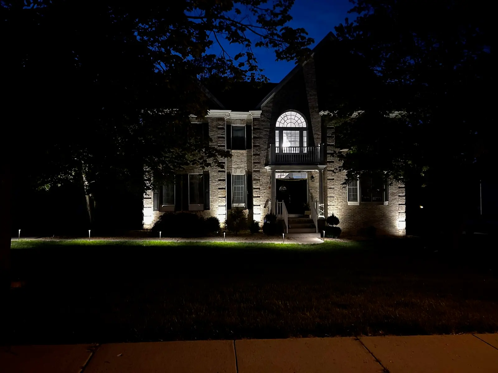 Brick colonial home with landscape uplighting and pathway lighting at night