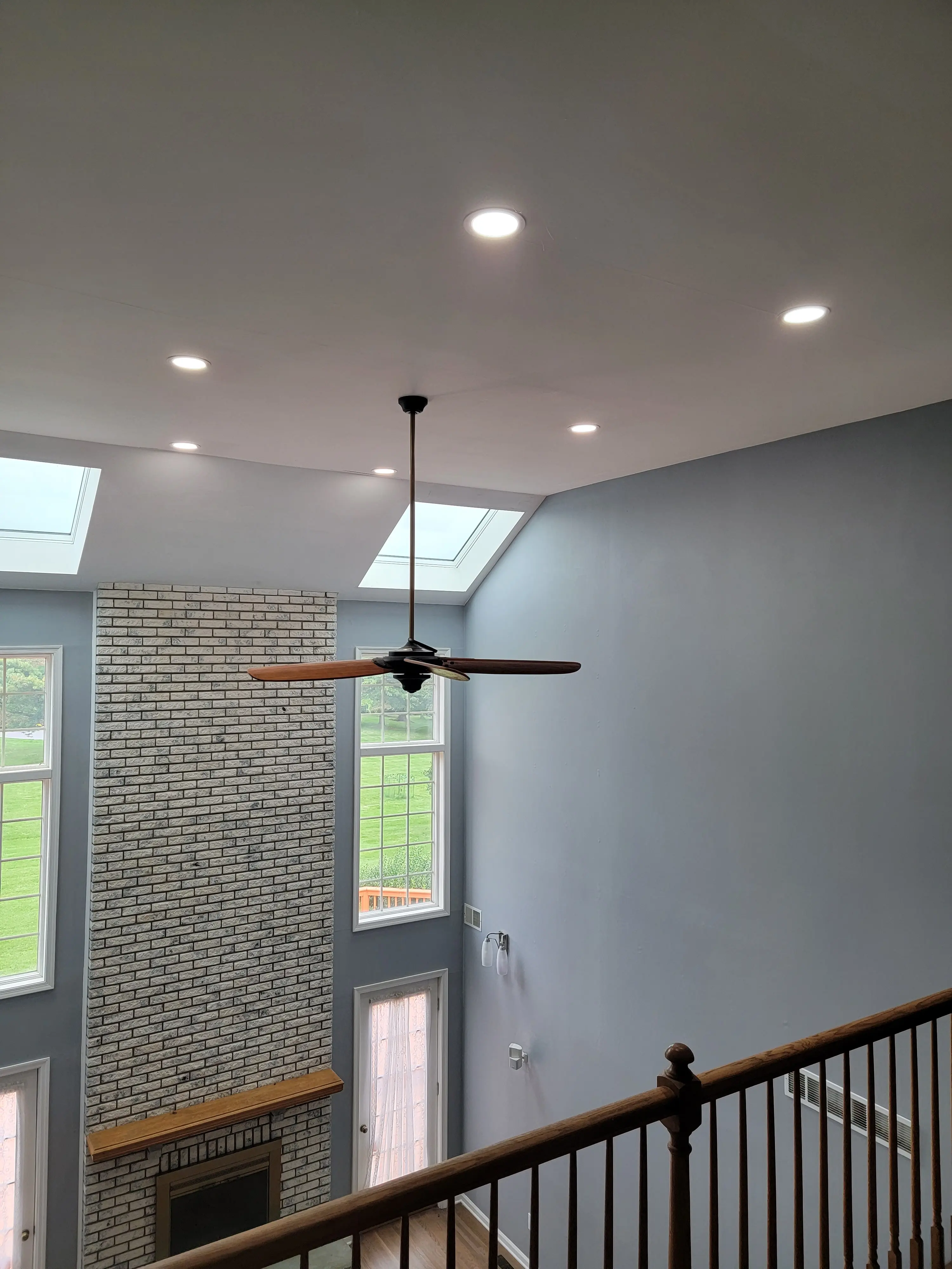 Tall residential living space with recessed ceiling lighting, skylights, a ceiling fan, and a brick fireplace